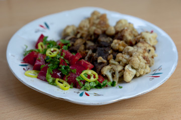 Tasty lunch on a plate. Fried meat slices, cauliflower, hot peppers, tomatoes, parsley