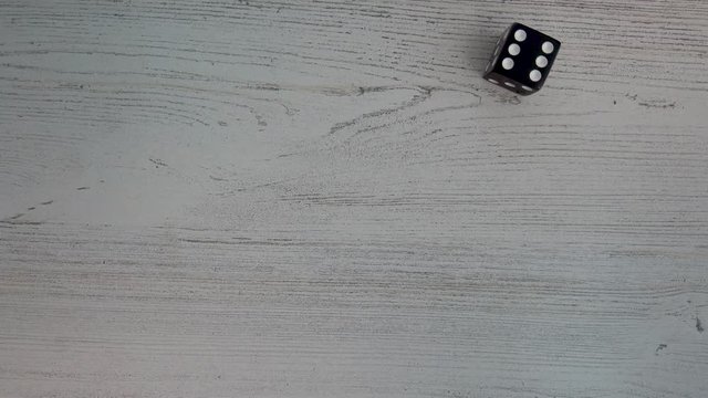 Hand rolls black dice, and lands a 6 on white wooden background.