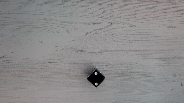 Six sided black die on white background rolls a 2, closeup, flat lay 4k slow.