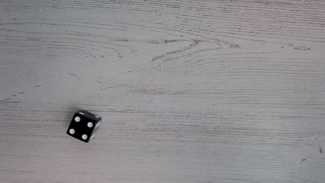 4k, slow motion closeup of a black six sided dice landing on four.