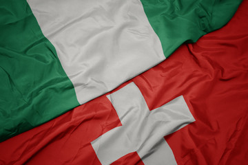 waving colorful flag of switzerland and national flag of nigeria.