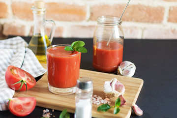 Tomato juice in a glass and fresh tomatoes on wooden table. Salt and garlic for dressing.