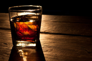 Cola with whiskey and ice on a wooden table background
