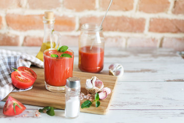 Tomato juice in a glass and fresh tomatoes on wooden table. Salt and garlic for dressing.