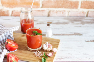 Tomato juice in a glass and fresh tomatoes on wooden table. Salt and garlic for dressing.