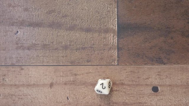 Hand rolls a 2 on a 10 sided white die on wooden background. 4k top down, slow.