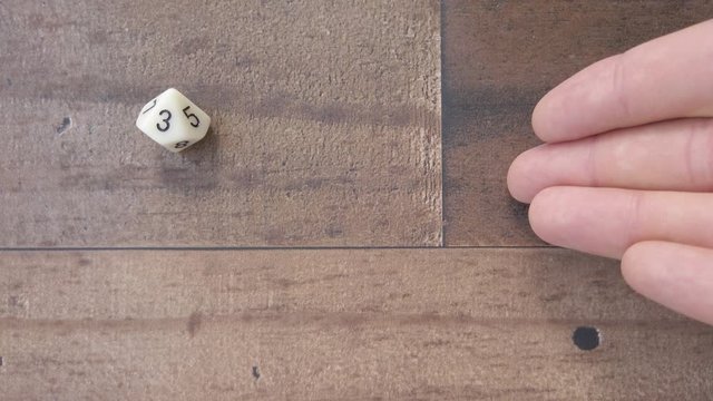 Hand rolled a 10 sided dice on brown wood, rolls a 3. 4k, flat lay closeup.