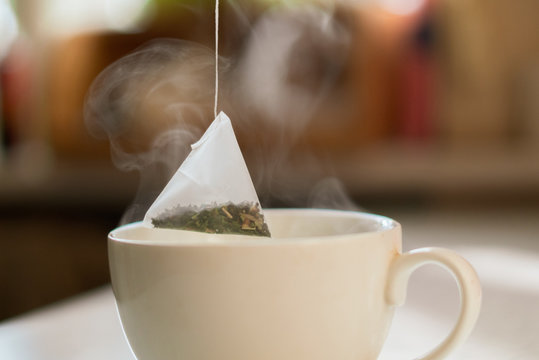 hand putting a pyramid tea bag in a hot water cup in the morning