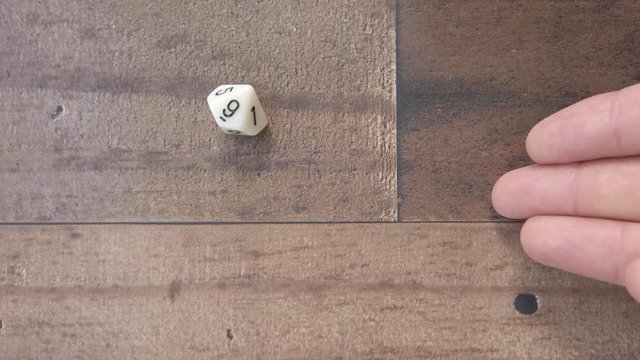 White nine sided die rolled by hand lands on nine. Wood background, 4k top down.