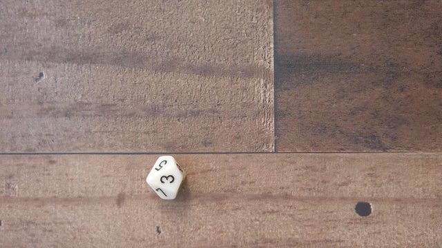 Hand rolled a 3 on a 10 sided die. Closeup, flat lay, 4k, slow motion.