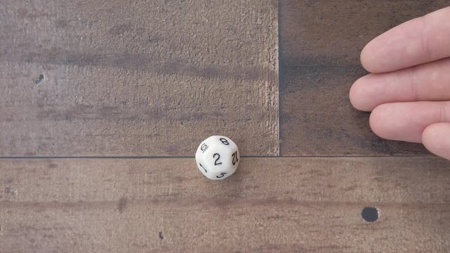 Twelve sided die, on wooden background, hand rolls a two. Flat lay, 4k slow.