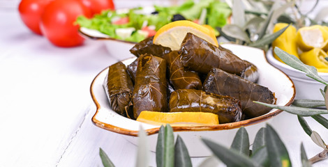 Traditional greek cuisine. Wrapped rice in grape leaves. Dolma with lemon and spices. Home cooked food. Olive branches and various spicy appetizers.