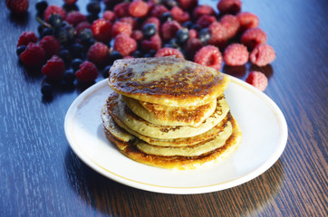 Pancakes with berries and maple syrup with raspberries and blueberries on a black background