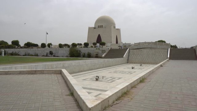 Karachi Mazar-e-Quaid Jinnah Mausoleum Frontal View with Empty Fountain and Waving Pakistan Flag on a Cloudy Day