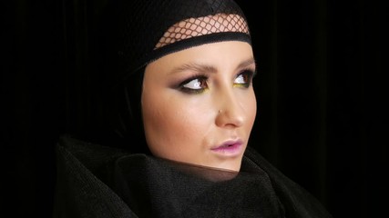 Professional girl model with beautiful makeup poses in a black cap on her head in front of the camera on a black background in the image of a black widow. High-fashion