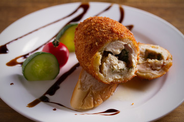Chicken Kiev and vegetables on white plate, wooden background. Breaded chicken breast stuffed with herbs and butter