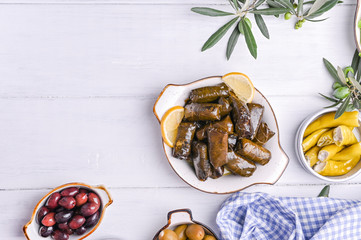 Traditional greek cuisine. Wrapped rice in grape leaves. Dolma with lemon, spices, various pickled olives and hot peppers. Fresh branches and homemade food.