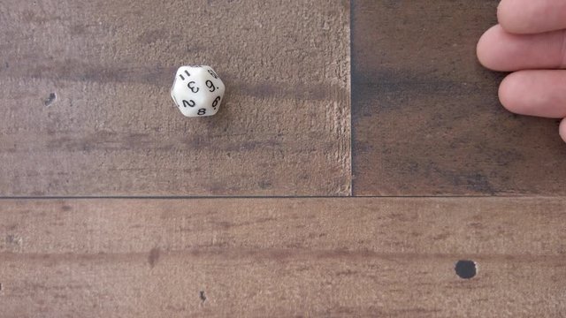 D20 hand rolls and lands on 3. Brown wood table or floor, playing a game, 4k.
