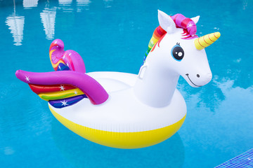 Rainbow coloured inflatable unicorn floating in a swimming pool in the summer, vivid blue water with contrasting white and multicolored unicorn