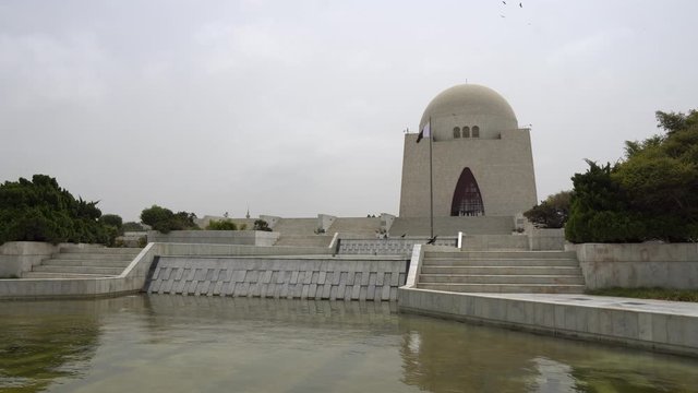 Karachi Mazar-e-Quaid Jinnah Mausoleum Frontal View with Pond and Waving Pakistan Flag on a Cloudy Day