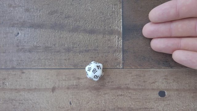 Hand rolls a 18 on 20 sided white die. 4k, flat lay, closeup, wood background.