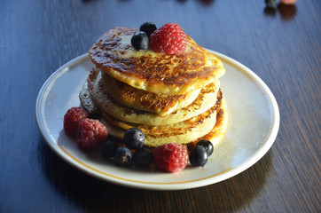 Pancakes with berries and maple syrup with raspberries and blueberries on a black background
