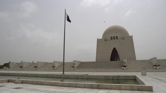 Karachi Mazar-e-Quaid Jinnah Mausoleum Frontal View with Pond and Waving Pakistan Flag on a Cloudy Day