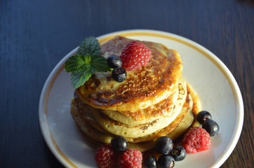 Pancakes with berries and maple syrup with raspberries and blueberries on a black background
