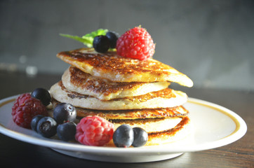 Pancakes with berries and maple syrup with raspberries and blueberries on a black background