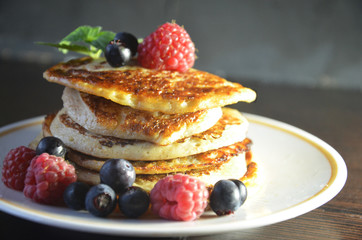Pancakes with berries and maple syrup with raspberries and blueberries on a black background