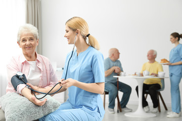 Obraz premium Nurse measuring blood pressure of elderly woman at retirement home. Assisting senior people