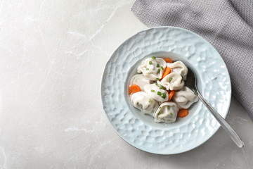 Plate of tasty dumplings in broth with spoon on grey marble table, top view. Space for text