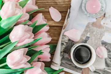 Background with bouquet of pink tulips on brown wooden boards with cup of coffee. candle and magazine. Top view. Toned image. Horizontal