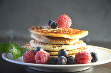 Pancakes with berries and maple syrup with raspberries and blueberries on a black background