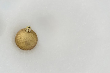 A sparkling golden Christmas ball lies in the winter white snow. There is a place for text.
