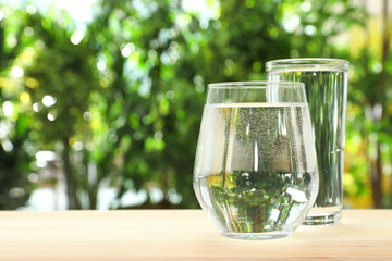 Glasses of water on table against blurred background, space for text. Refreshing drink