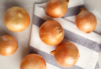Ripe onions and fabric on grey table, flat lay