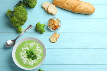 Flat lay composition with bowl of cheese cream soup and broccoli on blue wooden table. Space for text