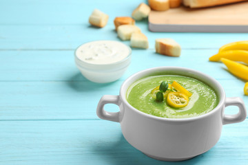 Bowl of broccoli cream soup with chili pepper served on blue wooden table. Space for text