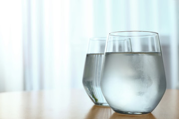 Glasses full of water on wooden table in room, space for text. Refreshing drink