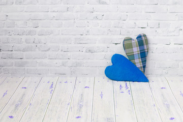 Two handmade hearts from checkered fabric stand on a light brick background, and on a light background of a wooden table . The concept of love, congratulation, manual labor needlewoman.