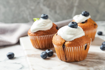 Marble board with tasty muffins, cream and blueberries on table