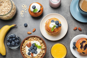 Different tasty dishes with blueberries on grey table, flat lay