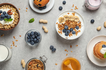 Different tasty dishes with blueberries on grey table, flat lay