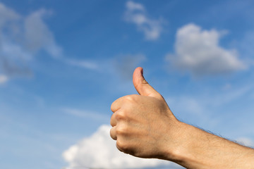 Man's hand shows thumbs up sign on blue sky background