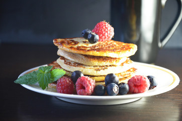 Pancakes with berries and maple syrup with raspberries and blueberries on a black background