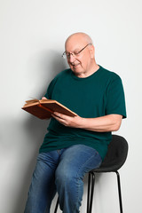 Portrait of senior man with glasses reading book on light background