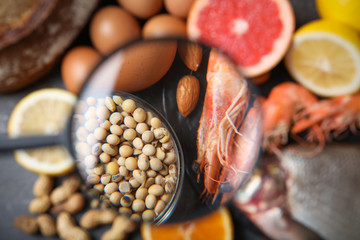 Different products with magnifier focused on soy beans and shrimps, closeup. Food allergy concept