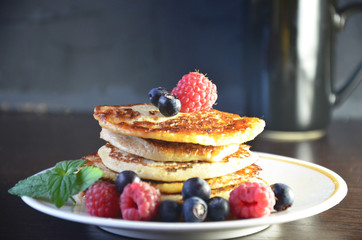 Pancakes with berries and maple syrup with raspberries and blueberries on a black background