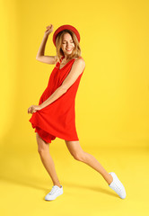 Beautiful young woman in red dress dancing on yellow background